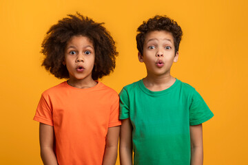 African American boy and girl are standing side by side with their mouths wide open in a look of...