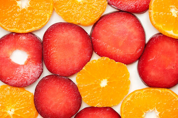 Thinly sliced fruit, bright red plums and oranges on white background
