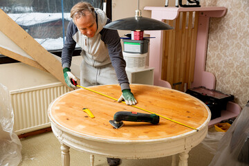 Middle-age man upcycling old wooden table using electric sander. Furniture restoration, DIY repair, repair by oneself and home improvement. Recycling and sustainable lifestyle