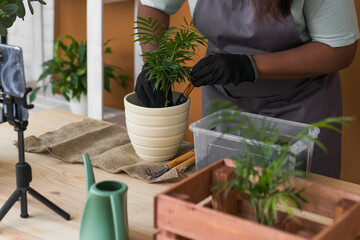 African american florist blogger filming tutorial video about transplanting plants in home garden. Make video vlog with mobile phone