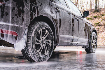 Vehicle covered in white soapy foam during regular carwash outdoors, auto getting professional wash...