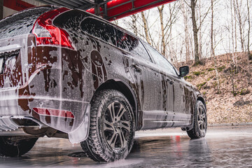 Vehicle covered in white soapy foam during regular carwash outdoors, auto getting professional wash...