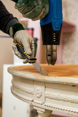 Middle-age man upcycling old wooden table using heat gun for removing old pain. Furniture...