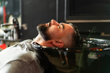 A man relaxes during a professional beard wash at a modern barbershop, highlighting meticulous...
