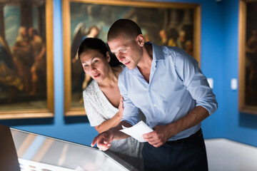 Adult man and woman watching exposition in gallery hall