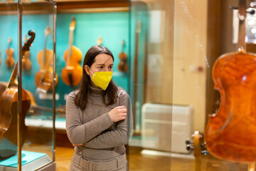 Portrait of interested adult brunette wearing protective face mask visiting exhibition of medieval...