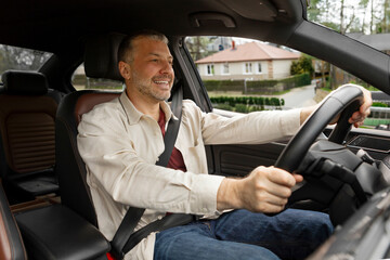Happy car owner. Middle aged man holding automobile wheel, testing new vehicle or sitting in own...