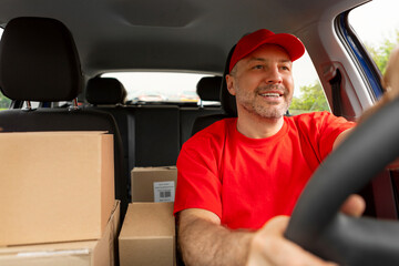 Obraz premium Happy middle aged man courier driving car and smiling. Delivery and shipping concept