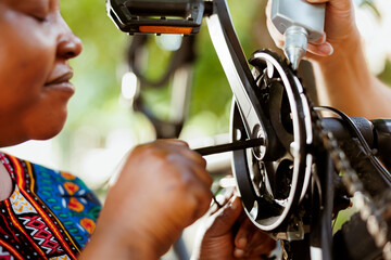 Close up of female african american using allen key to repair damaged bicycle crank-arm. Outdoor detailed shot of two people repairing and greasing bike chain and pedals for secure outdoor cycling.