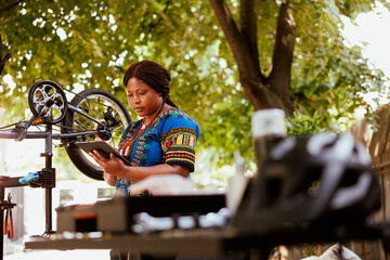 Healthy active female cyclist grasping smart device with instructions for fixing bicycle. Sporty...