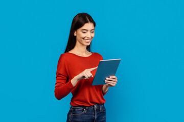 Fototapeta premium A woman wearing a red shirt is holding a tablet in her hands. She is looking at the screen intently, seemingly engaged with the device.