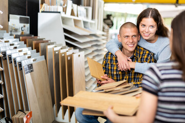 Competent seller consulting young couple about purchase of laminate flooring in building store