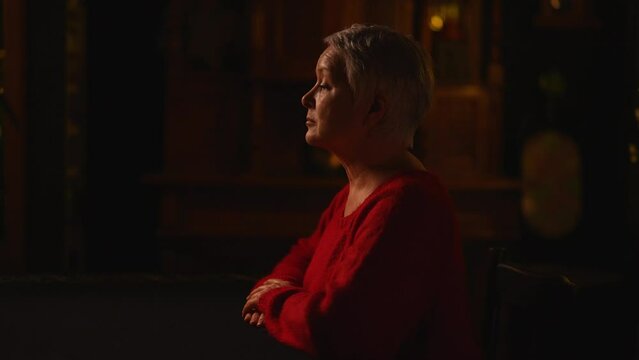 Sad unhappy middle-aged woman sitting at table while listening negative prediction from unrecognizable fortune teller in dark esoteric room with mystical atmosphere. Concept of divination, magic.