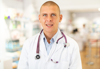 Portrait of male pharmacist in white coat standing in chemist shop.