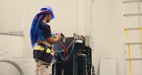 Skilled african american expert looking at freon levels in air conditioner while using manifold...