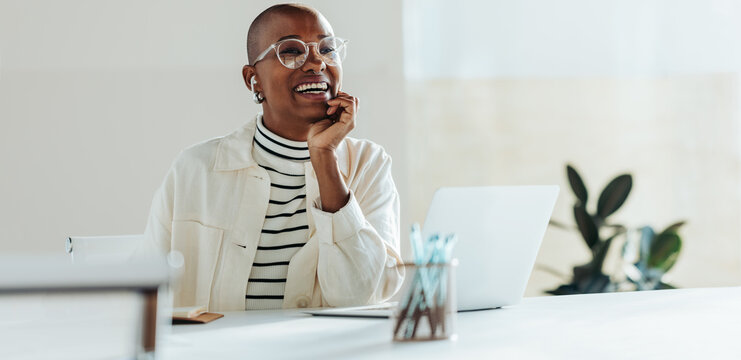 Joyful businesswoman with glasses laughing in a bright office setting, modern workplace, positive work environment
