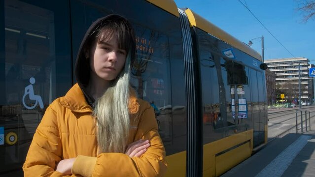 Sad girl wait by tram. A sad young girl stand in the road against yellow tramway.