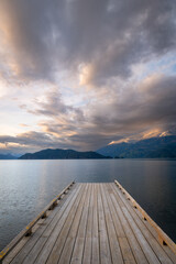 Obraz premium Wooden boat dock leading out to a lake with calm waters with a sunset sky. Harrison Lake, east of the lake are the Lillooet Ranges while to the west are the Douglas Ranges, British Columbia, Canada. 