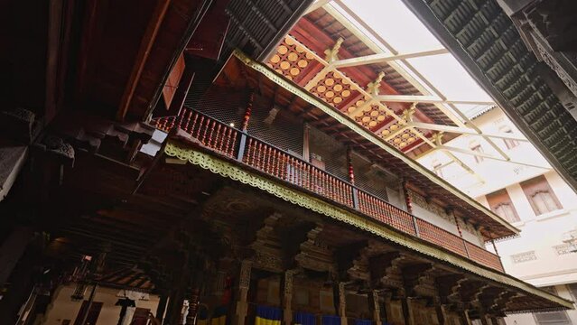 Interior of Sri Dalada Maligawa with rich wood carvings, ornate pillars, religious artifacts. Sunlight streams through rooftop, illuminating sacred Buddhist temple in Kandy. Visitors seek serenity.
