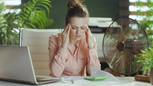 Sustainable workplace. unhappy modern female worker at work with electric fan.