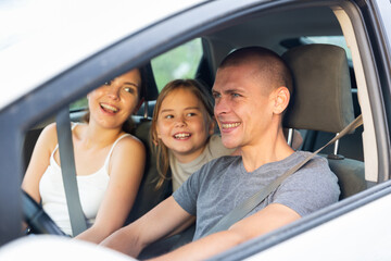 Positive young adult man driving car during trip with his family, woman and little girl