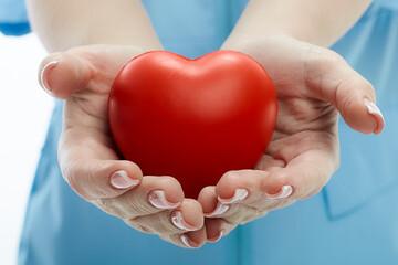 A red heart in the hands of a young woman doctor