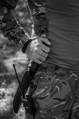 A soldier with a walkie-talkie pulls out a military knife from a scabbard attached to his...