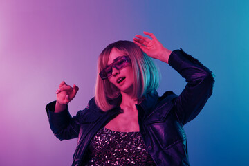 Sexy beautiful blonde lady in leather jacket sparkly dress trendy sunglasses dance hold hands up posing isolated in blue pink color light studio background. Neon party Cyberpunk concept. Copy space