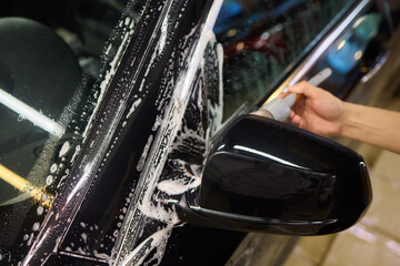 A person is cleaning a car windshield with a brush and water