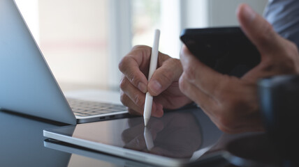 Businessman signing digital document on digital tablet and working on laptop computer on office table, e-signing. Business man using mobile phone and tablet pc