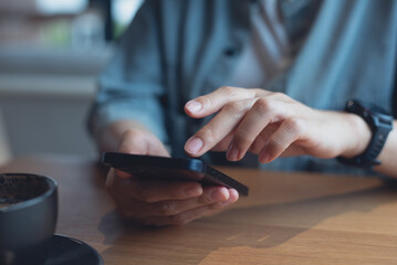 Close up of, woman sitting at wooden table using mobile phone in coffee shop, finger touching on phone screen. Woman using smartphone for mobile banking, online shopping, social media network