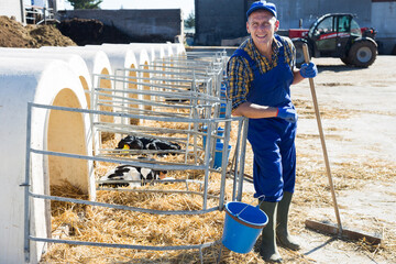 Farmer in workwear standing beside outdoor calf pen, looking in camera and smiling.