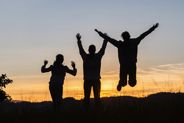 Three people jumping on mountain sunset sky background.