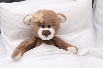 Toy cute bear with sticking plaster under blanket in bed