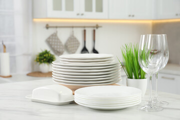 Clean plates, glasses, butter dish and floral decor on white marble table in kitchen