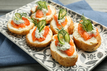 Tasty canapes with salmon, cucumber, cream cheese and dill on wooden table, closeup