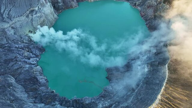 Aerial view Drone shot of fog at Kawah Ijen volcano with turquoise sulfur water lake and sunrise light.Amazing nature landscape view at East Java,Indonesia.Beautiful light Natural landscape background