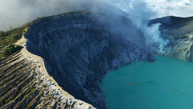 Aerial view Drone shot of fog at Kawah Ijen volcano with turquoise sulfur water lake and sunrise light.Amazing nature landscape view at East Java,Indonesia.Beautiful light Natural landscape background