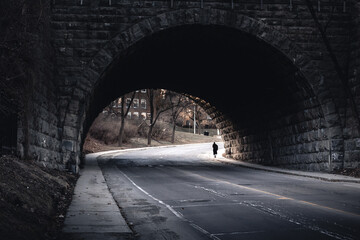 Person walks under dark bridge with tints of monochrome landscape