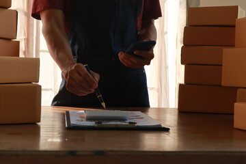Middle aged Asian man, the owner of a small business, happily works on her laptop at home. She's managing orders and packaging products for delivery, showcasing success in e-commerce.