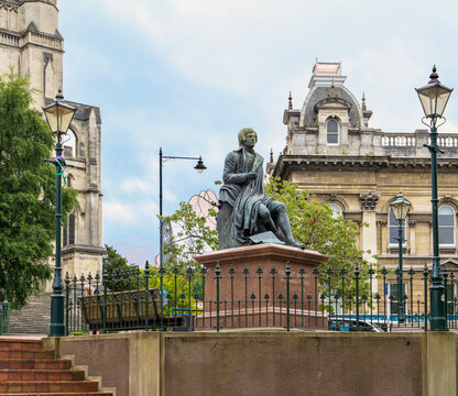 Dunedin, New Zealand - 9 September, 2023: Bronze statue of Robert Burns seated, overlooking the Octagon with St Pauls Cathedral and the ornate Dunedin Town Hall in the background
