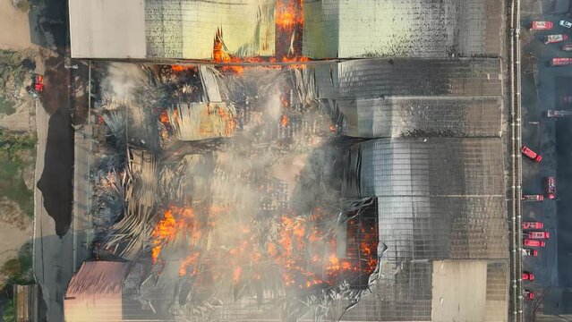 From the skies, witness the aftermath of a fierce blaze as it consumes a vast industrial structure, leaving behind a landscape tainted by smoke and ruin, underscoring the impact of air pollution.
