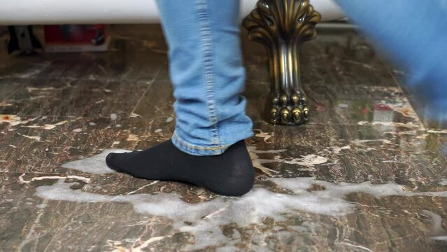 Man in jeans steps in spilled liquid on floor closeup. Male in socks slips on floor almost falling against sofa legs in modern appartment