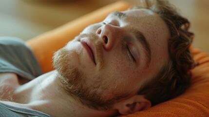 A man lying on his side in a supported twist pose with a bolster under his head and a sense of relief on his face as he releases tension and emotions.