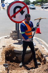 african american worker with a pickaxe digging a ditch in the highway to repair cabling on an isle...