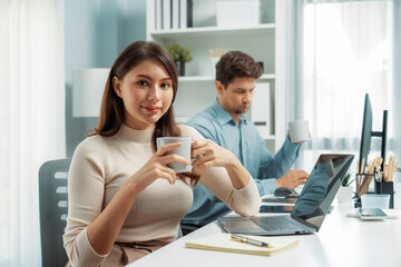 Smiling beautiful woman holding coffee cup to pose for looking at camera photo shooting portrait profile's business, working with smart coworker at modern office at morning on working desk. Postulate.