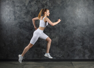 young sportswoman in white sportswear run near black marble wall