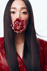 Attractive woman with long black hair in red jacket holding flower in mouth, isolated on white...