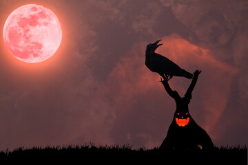 The silhouette of a crow standing on a demonic tree in the atmosphere of a terrifying red full moon.