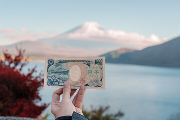 Hand holding 1000 yen banknote with mount Fuji at Lake Motosu, happy tourist travel Mt Fuji and...
